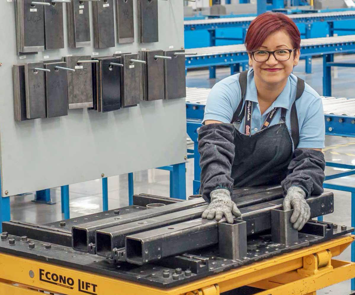 A photo of the inside of Corefficient’s quality control lab, an attractive red-haired woman in a safety apron and protective gloves smiles at the camera as she leans over products.