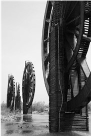 A black and white photograph of four old waterwheels, one up close on the right, furthest on the left.