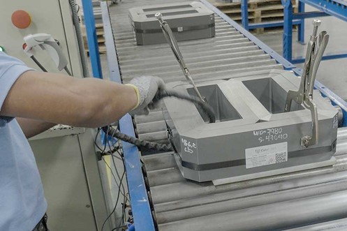 A worker wearing gloves assembles a DG core with clamps on an assembly line in a factory.