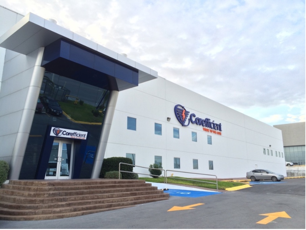 The front entrance of Corefficient’s headquarters on a sunny day in Monterrey, Mexico - showing the logo on the side of their modern building and a silver car parked in front.