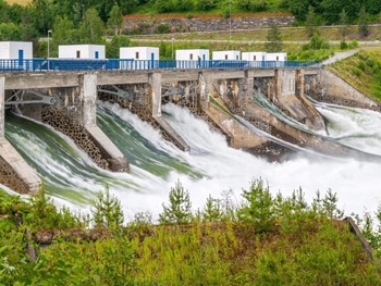 A side view of a hydroelectric power plant on a rushing river with green grass in the foreground.