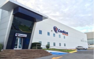 The front entrance of Corefficient’s headquarters on a sunny day in Monterrey, Mexico - showing the logo on the side of their modern building and a silver car parked in front.