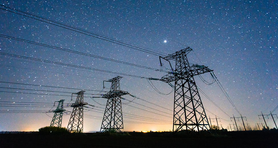 An AC electric grid at sunset: the landscape, grids, and wires are black, the yellow sun sets behind the horizon, and the night sky is above, filled with stars.