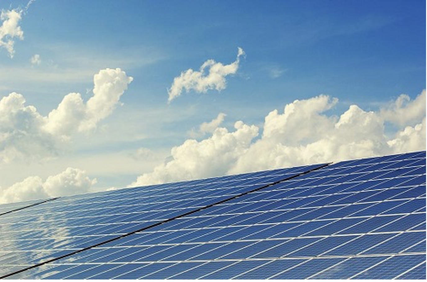 Solar panels on a sunny day with some clouds in the blue sky behind the panels.