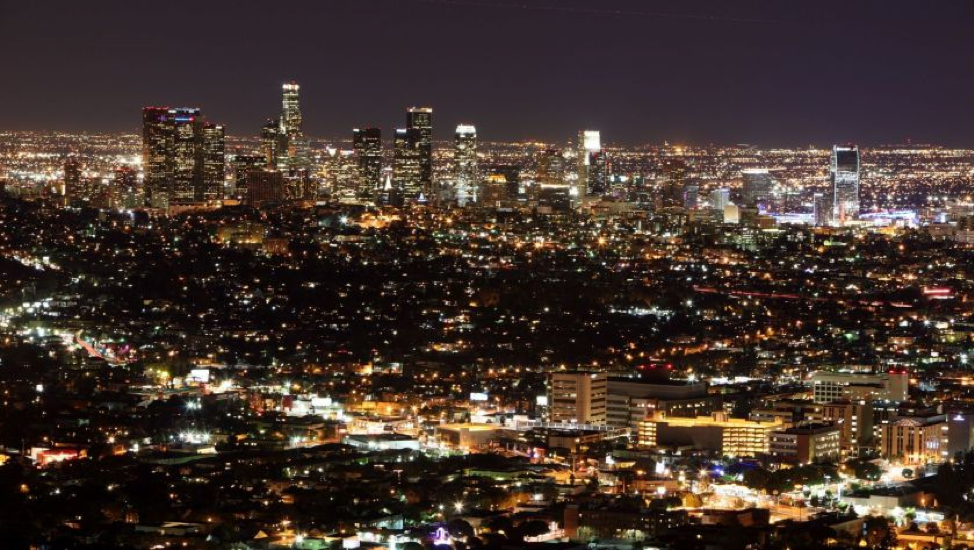 A view of downtown Los Angeles at night. The city is aglow with electrical light all the way to the horizon line.