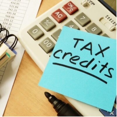 A calculator and notes on top of a table. A post-it note is placed on top of the calculator with a message that reads 'Tax Credits,' where the word 'Credits' is underlined.
