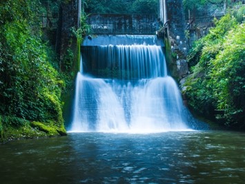 Hydropower waterfall framed by lush greenery and a pool of water in the foreground.
