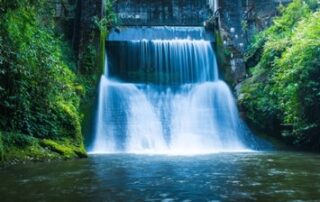 Hydropower waterfall framed by lush greenery and a pool of water in the foreground.