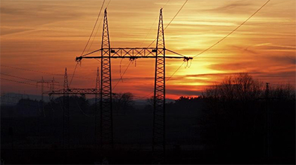 Power lines extending through a forest landscape at sunset.